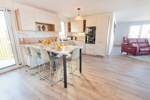 A modern kitchen with a dining area, a red sofa, and a large window. - Premium 3-bedroom apartment with a view of Lorient Roadstead – by Groom* (Lorient)