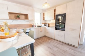 A modern kitchen with light wood cabinets, a marble countertop, and a built-in oven. - Premium 3-bedroom apartment with a view of Lorient Roadstead – by Groom* (Lorient)