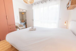 Een slaapkamer met een groot bed, een houten garderobe, een bureau met stoel en een raam met gordijnen.