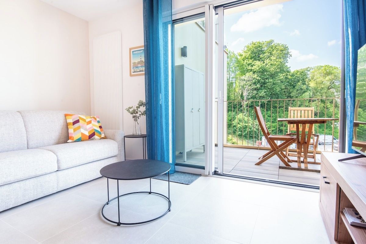A modern living room with a sofa, a small round table, and a balcony with a wooden table and chairs.