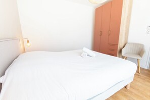 Ein Schlafzimmer mit einem großen Bett, einem Kleiderschrank, einem Sessel und einer Nachttischlampe.