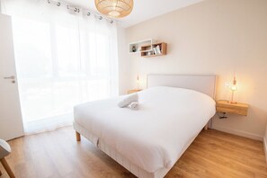 Een slaapkamer met een groot bed, nachtkastjes, een plank met boeken en een raam met gordijnen.