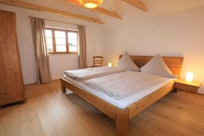 A wooden bed with a headboard, a bedside table with a lamp, a window with curtains, and a wooden wardrobe. - ||-------------------------------House of Heaven--------------------------|| (Oberammergau)