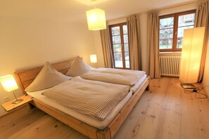 A room with a wooden bed, two bedside lamps, a window with curtains, and a radiator. - ||-------------------------------House of Heaven--------------------------|| (Oberammergau)