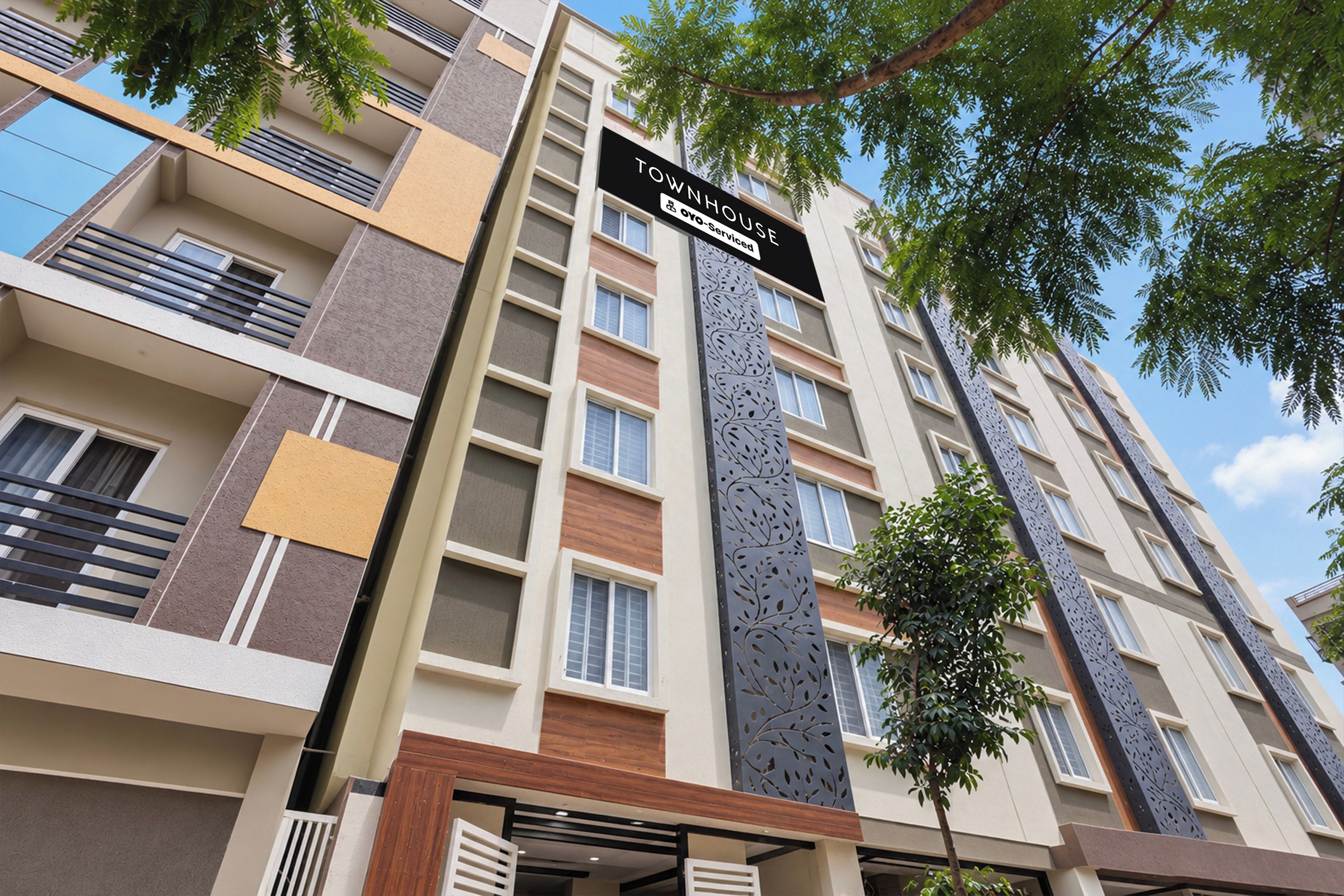Un edificio residencial de varios pisos con balcones, un cartel que indica que cuenta con servicios y un árbol en primer plano.