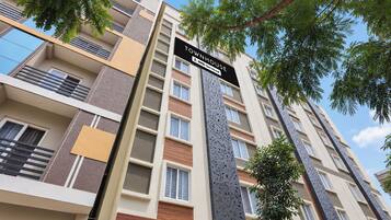 Un edificio residencial de varios pisos con balcones, un cartel que indica que cuenta con servicios y un árbol en primer plano.