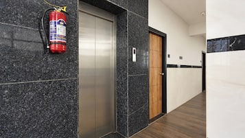 Un pasillo con extintor montado en la pared, una puerta y un panel de control de ascensor fijado a la pared.