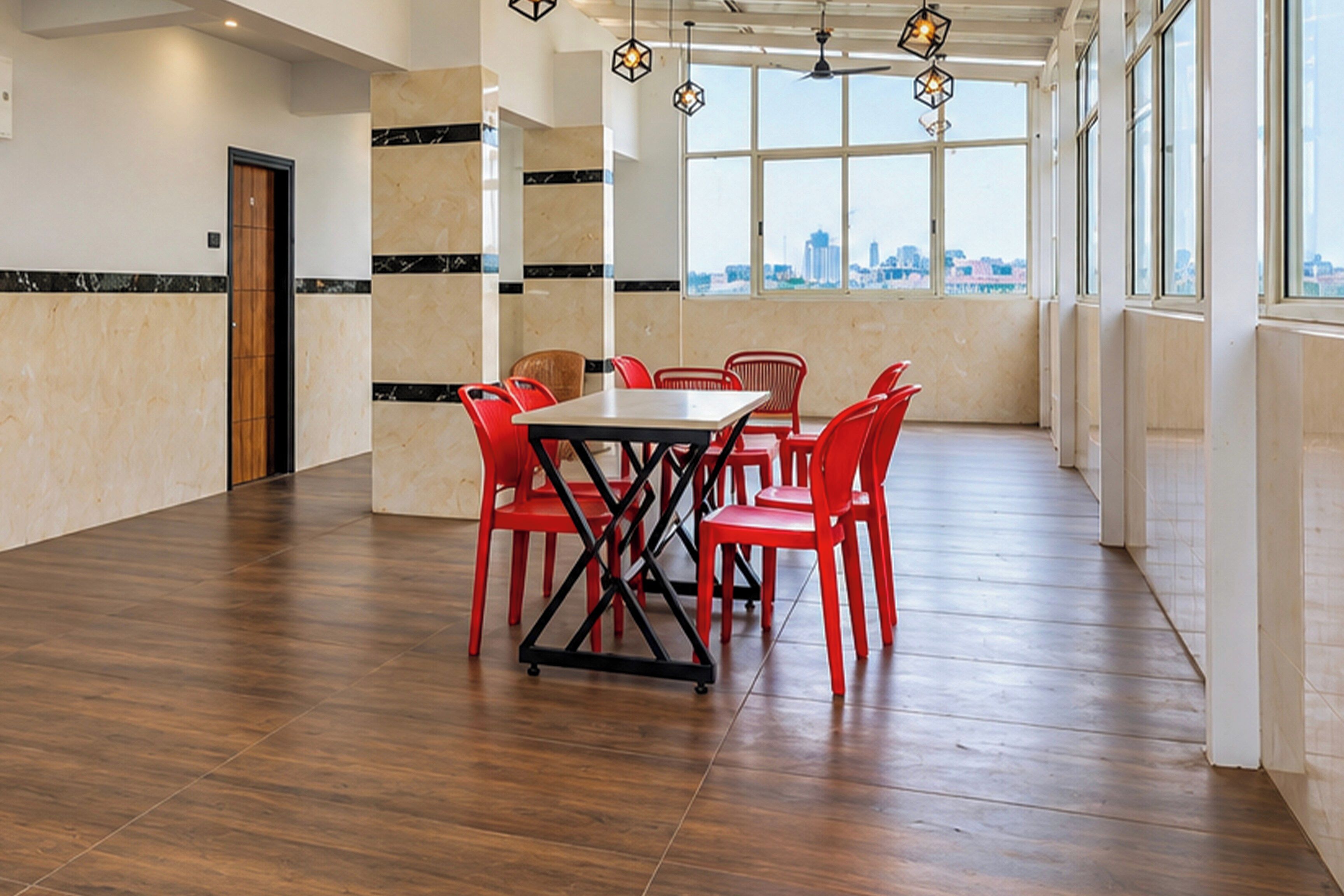Una habitación amplia con suelo de madera, una mesa central con sillas y grandes ventanales que ofrecen vistas a la ciudad.