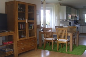 Een eetgedeelte met een houten tafel, stoelen, een kast met glazen deuren en een televisie op een dressoir.
