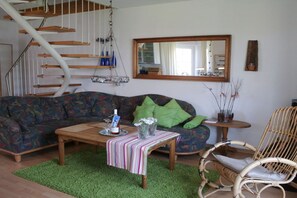 Ein Wohnzimmer mit einer Couch, einem Couchtisch, einem Korbstuhl, einem Hängesessel und einer Wendeltreppe.