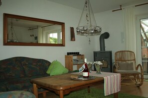 Ein Wohnzimmer mit einer Couch, einem Holztisch, einem Spiegel, einer Hängelampe und einem Kamin.