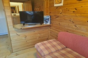A wooden interior with a television on a shelf, a plaid cushion, and a framed picture on the wall.
