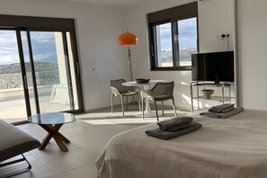 A modern hotel room with a bed, a dining table, chairs, a TV, and a view of the outdoors. - Holiday home in Pitsidia with swimming pool (Pitsidia)