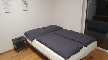 A bedroom with a single bed, a small bedside table, and a wall-mounted TV.