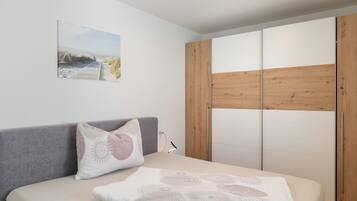 Een slaapkamer met een bed, een kussen, een nachtkastje, een lamp, een houten garderobe en een aan de muur hangend schilderij.