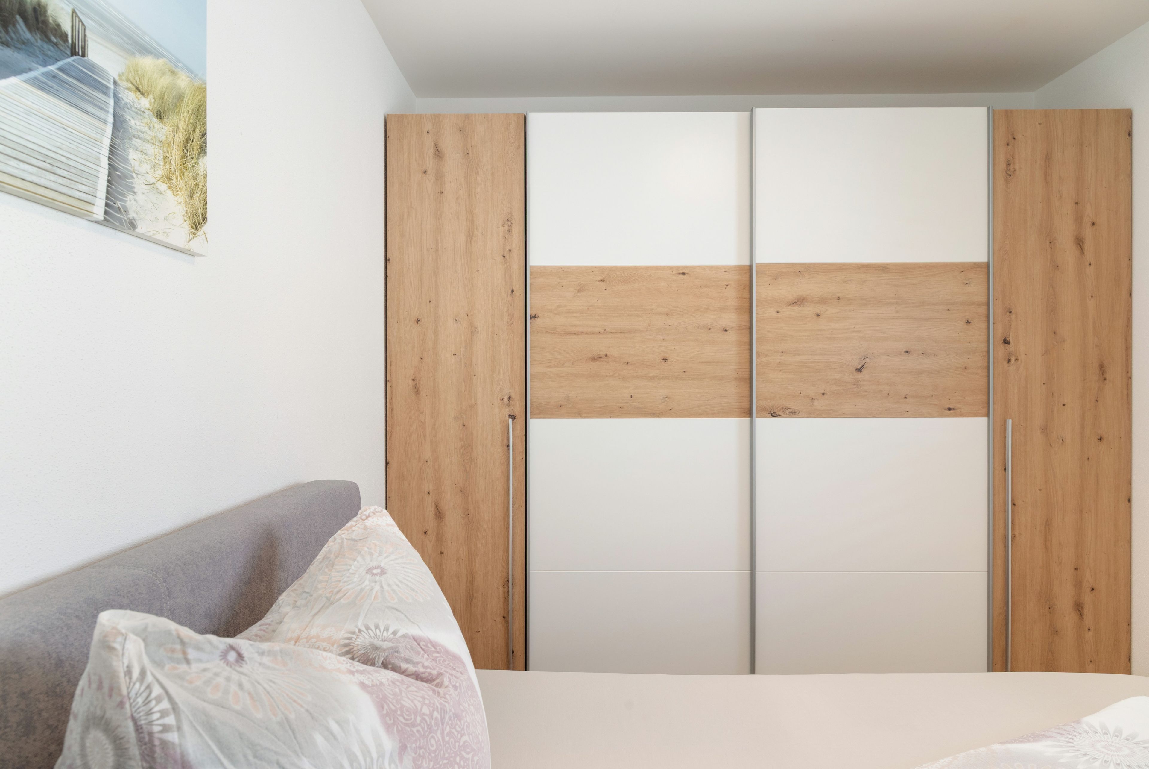 A bedroom with a bed, a grey sofa, and a wooden wardrobe with a white door.