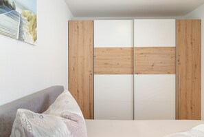 A bedroom with a bed, a grey sofa, and a wooden wardrobe with a white door.