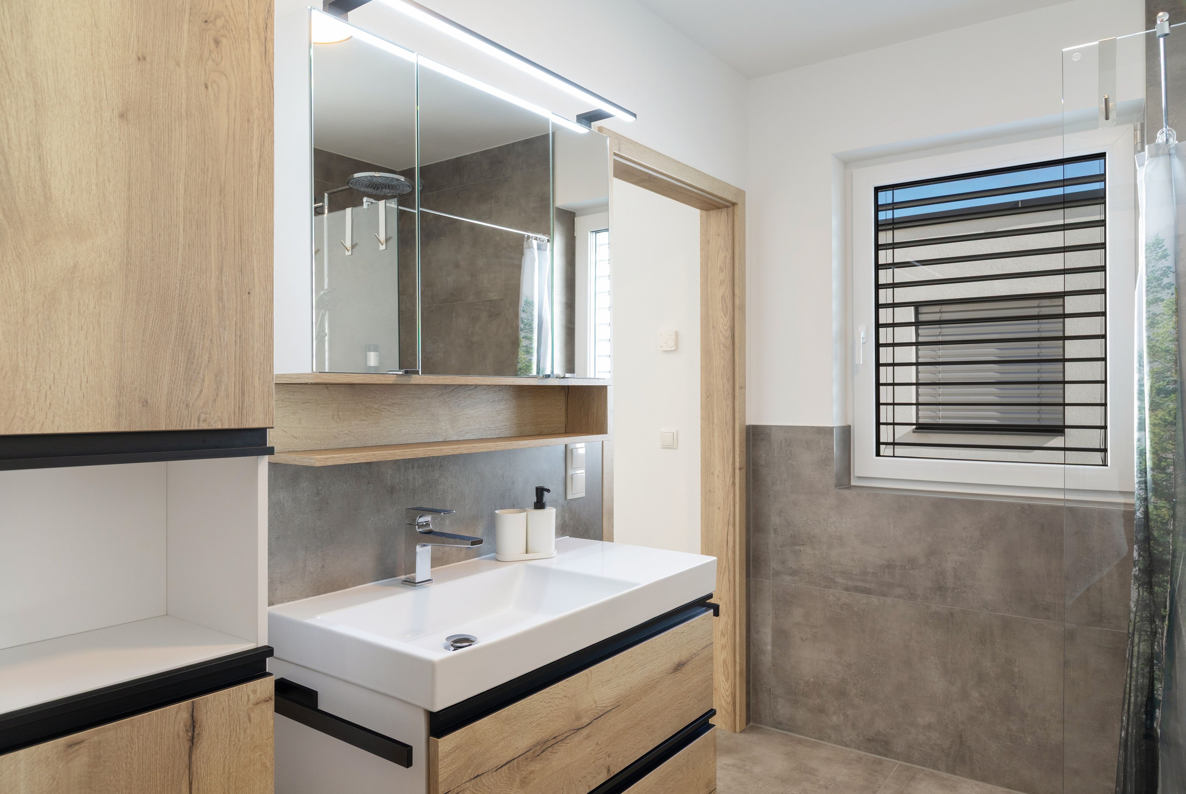 A modern bathroom with a white sink, wooden cabinetry, a mirror, and a shower with a glass door.