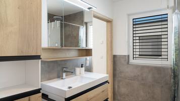 A modern bathroom with a white sink, wooden cabinetry, a mirror, and a shower with a glass door.
