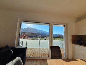 A room with a large sliding glass door leading to a balcony, a wooden table, a chair, and a sofa.