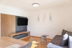 Una sala de estar moderna con un televisor de pantalla plana, listones de madera, un sofá gris y una obra de arte en la pared.