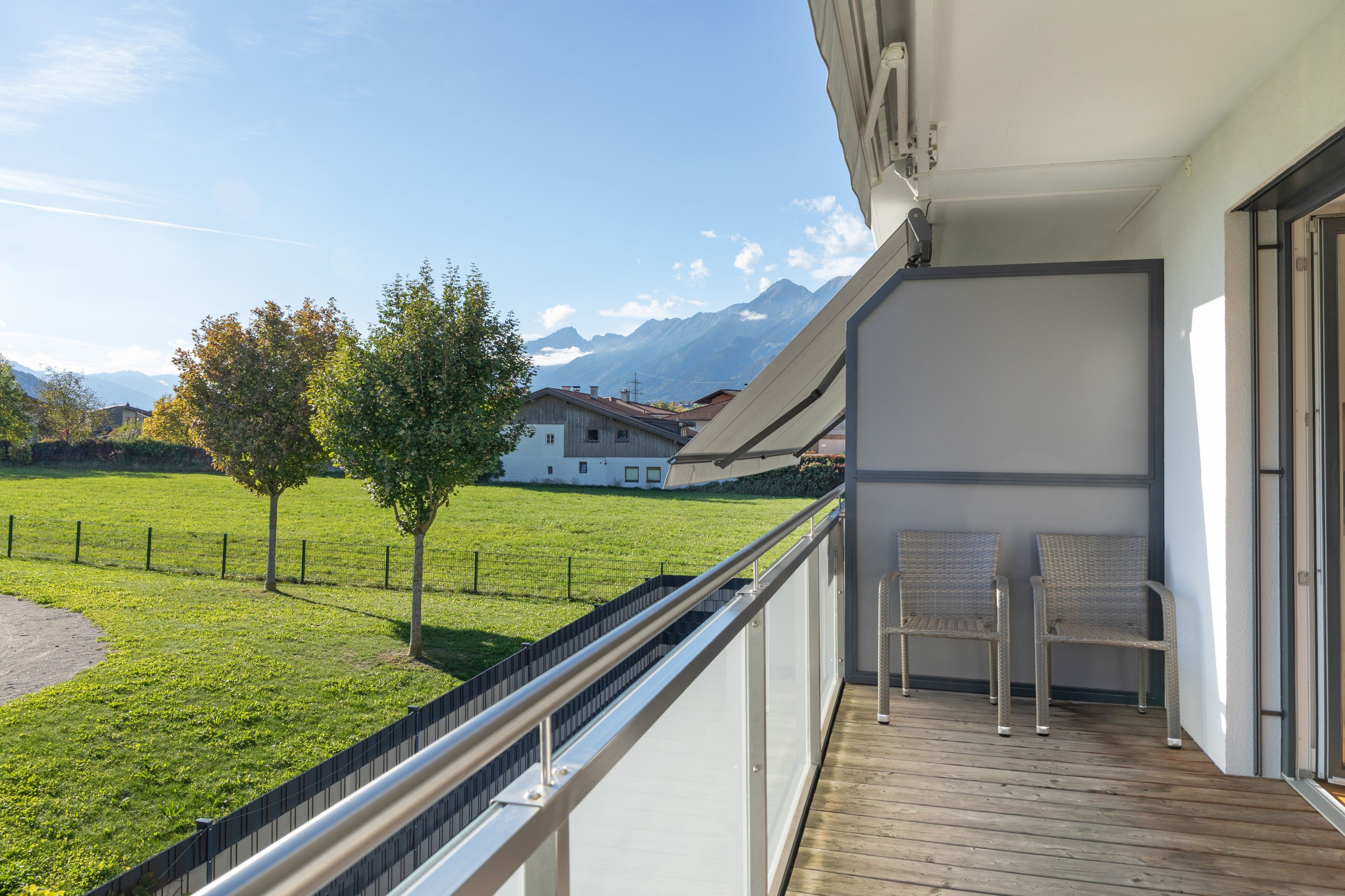Een balkon met uitzicht op een grasveld en bergen. Er staan twee stoelen op het balkon.