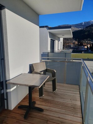 Un balcón con mesa y dos sillas, suelo de madera y vista a un paisaje montañoso.
