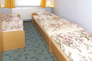 A single bed with a floral bedspread, a wooden headboard, and a window with yellow curtains. - Holiday apartment with 2 bedrooms (Neuschoo)