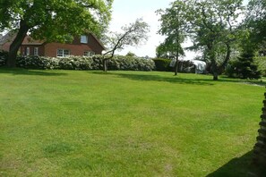 A grassy yard with a brick house and trees. - Holiday apartment with 2 bedrooms (Neuschoo)
