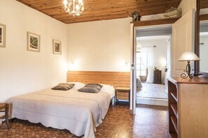 A bedroom with a wooden ceiling, a bed with a white bedspread, a nightstand, a lamp, and a mirror. - Gite Marie -Mas Paraloup (Lagorce)