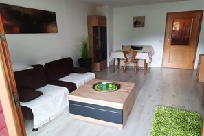 Ein Wohnzimmer mit einer Couch, einem Couchtisch, einem Esstisch mit Stühlen, einer Pflanze und einer Tür.