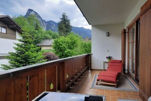 Ein Balkon mit einem roten Stuhl, Holzgeländer und Blick auf Berge.