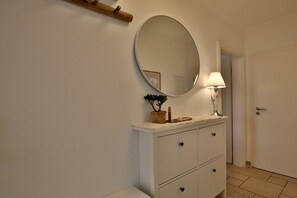 Een badkamer met een wit aanrichtmeubel, een ronde spiegel, een wandlamp en een kleine plant op het aanrichtmeubel.