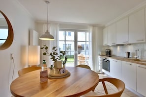 Een moderne keuken met witte kastjes, een ronde houten eettafel en een hanglamp.