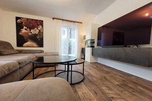 A modern living room with a sofa, a glass coffee table, a flat-screen TV mounted on a wall, and a painting on the wall. - Holiday home in Grainau with swimming pool (Grainau)