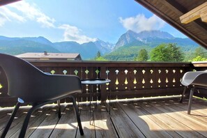 A wooden deck with two chairs and a small table, overlooking a mountainous landscape. - Holiday home in Grainau with swimming pool (Grainau)