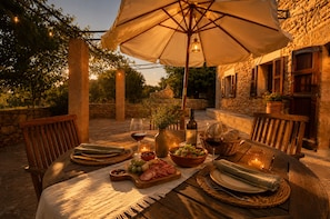An outdoor dining area with a table set for two, featuring a bottle of wine, glasses, bread, and a bowl of olives. - Finca Estilo Mallorquín Cerca del mar (Alcúdia)