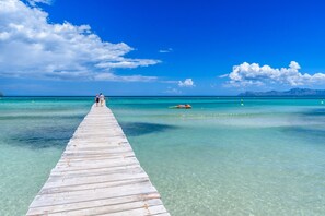 Eine Holzstege, der sich in klares türkisblaues Wasser erstreckt, mit blauem Himmel darüber.