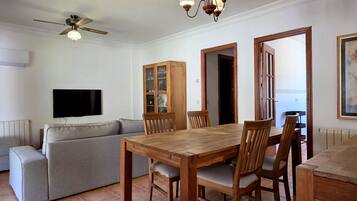 A living room with a sofa, wooden dining table, chairs, a ceiling fan, and a TV.