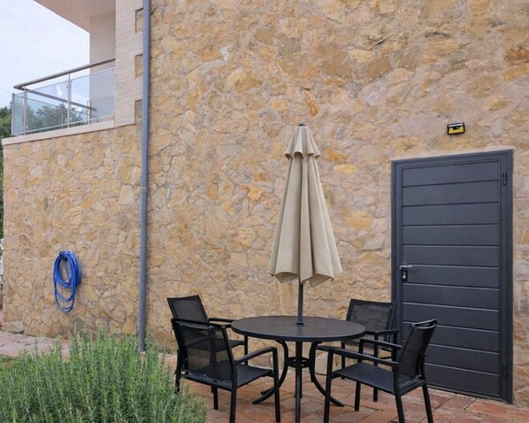 An outdoor seating area with a stone wall, a table with chairs, an umbrella, and a door.
