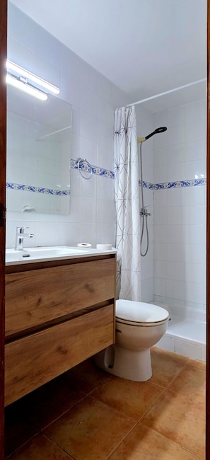 A bathroom with a wooden vanity, a white toilet, a shower with a curtain, and a mirror with a decorative tile border. - Chalet con Jardín Cerca de la Playa (Palma de Mallorca)