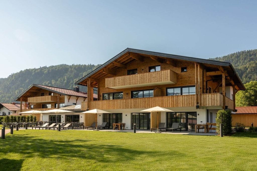 Un chalet moderne avec une façade en bois, de grands balcons et une pelouse bien entretenue.