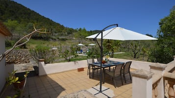 Une terrasse avec une table et des chaises, un parasol blanc et une vue sur une colline.