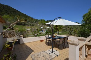Un patio con una mesa, sillas y una sombrilla blanca, con vistas a una colina.
