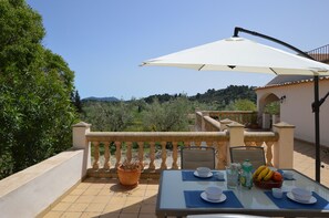 Eine Terrasse mit Frühstückstisch, einem Blumentopf und Blick ins Grüne.