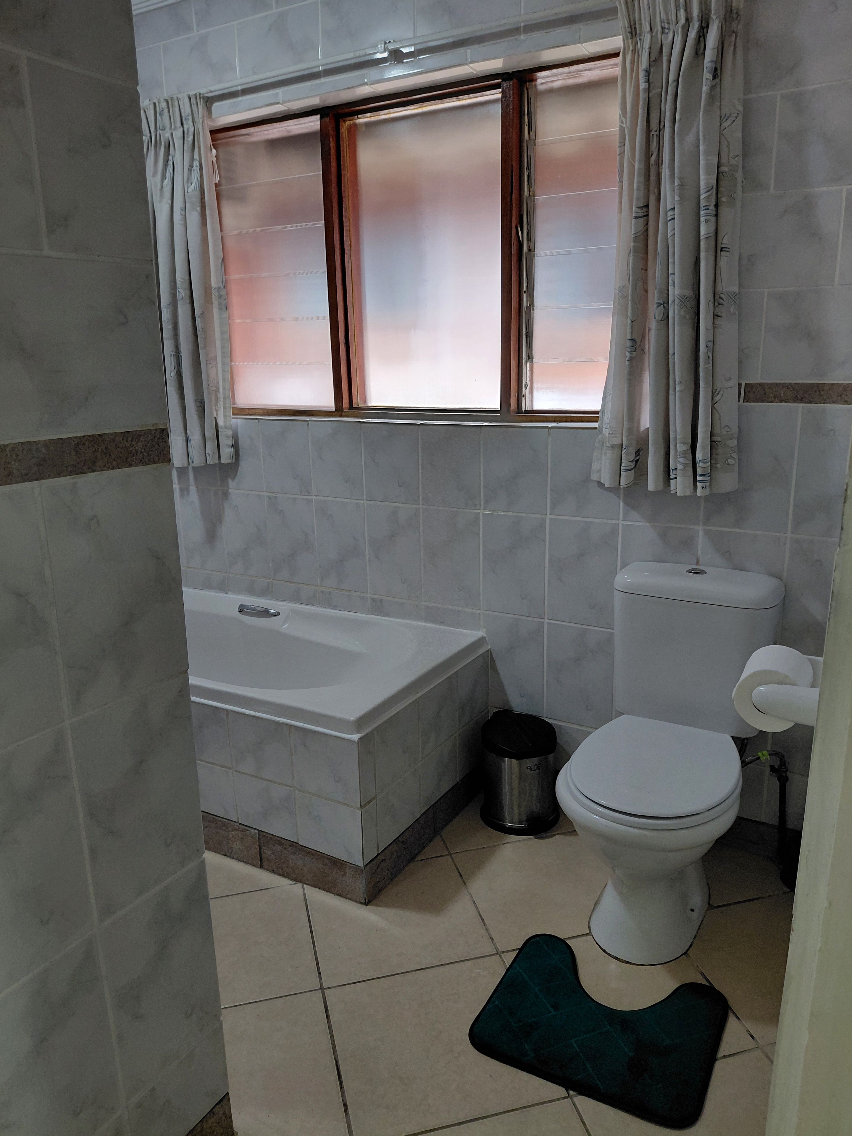 Ein Badezimmer mit Badewanne, Toilette und einem Fenster mit Vorhängen.