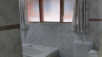 Ein Badezimmer mit Badewanne, Toilette und einem Fenster mit Vorhängen.