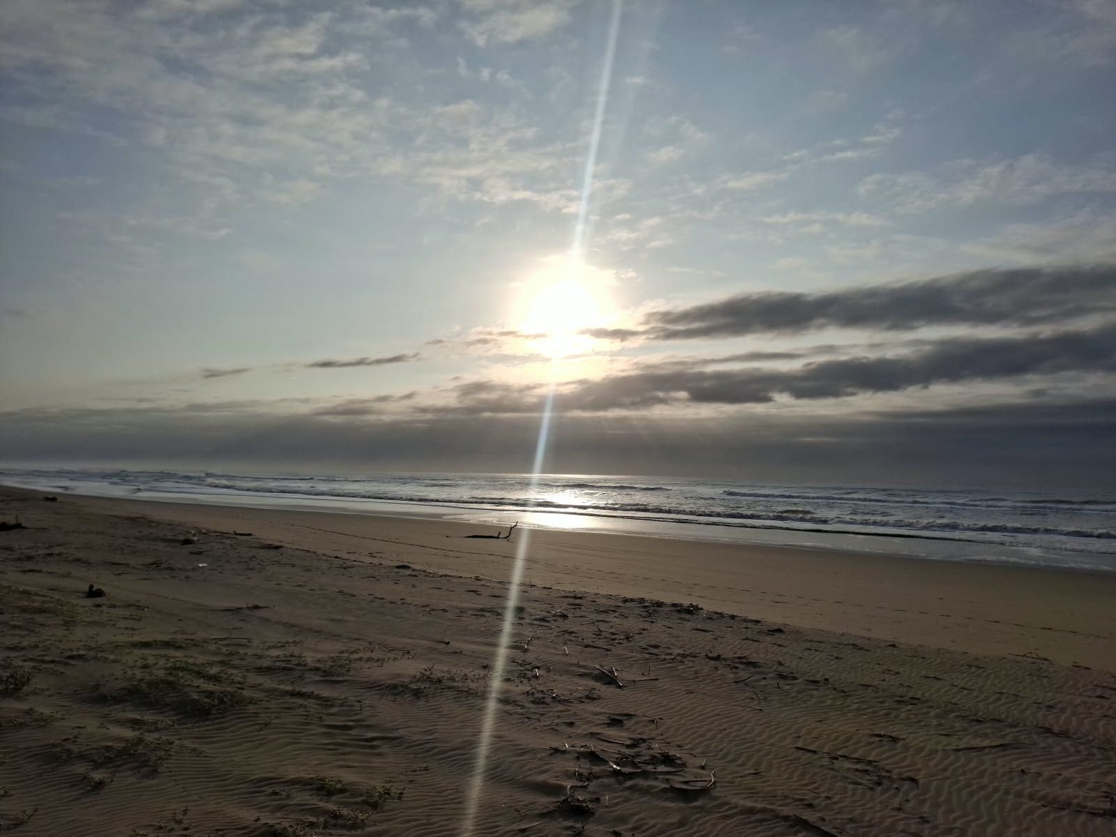 Ein Strand mit blauem Himmel und der Sonne, die sich im Wasser spiegelt.