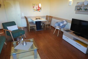 Un salon comprenant une table basse en verre, un canapé, un téléviseur et un coin repas avec des chaises et une table.