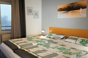A hotel room with a bed, a window with curtains, a wall-mounted picture, and a bedside lamp. - Holiday apartment with 2 bedrooms (Schillig)